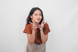 Adorable Asian woman in brown shirt making kissy face with pout lips and peace sign two fingers isolated on white background. photo