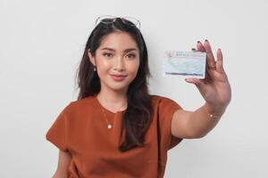 Confident young Asian woman wearing brown shirt is showing identity card Indonesia to the camera over white background. photo