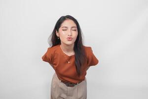 Cute Asian woman in brown shirt sending blowing kiss with pout lips looking at camera isolated on white background. photo