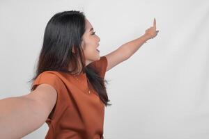 Young Asian woman in brown t-shirt doing call pose while pointing to the copy space behind her isolated over white background. photo