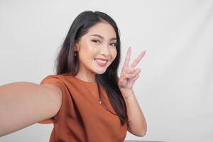 Happy Asian woman in brown t-shirt doing call pose while holding two fingers or peace sign isolated over white background. photo