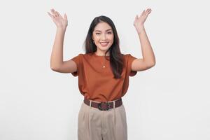 Excited Asian woman wearing brown shirt pointing to the copy space upside her, isolated by white background. photo