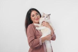 Lovely Asian woman wearing eyeglasses holding her ragdoll cat and smiling to the camera isolated over white background. photo