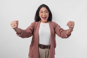 Cheerful young Asian woman in doing a successful win gesture with clenched fist over isolated white background. photo