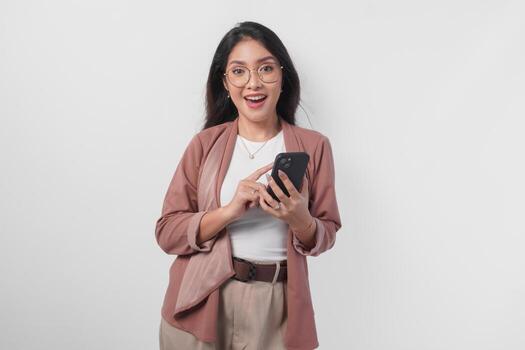 Smiling Asian woman in eyeglasses using phone to text or browse internet, isolated by white background. photo