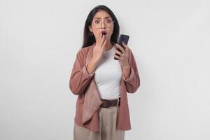 Shocked Asian business woman in eyeglasses pointing to her smartphone, isolated by white background. photo