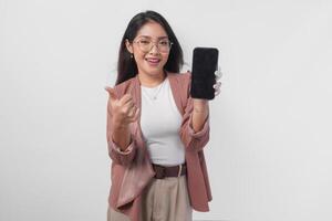 Excited Asian woman wearing eyeglasses gives thumbs up hand gesture of approval while showing copy space on her phone. photo