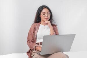 pensativo joven asiático negocio mujer sentado abajo con un ordenador portátil pensando acerca de trabajar, aislado por blanco antecedentes. foto