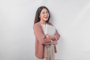 Attractive young Asian business woman holding a laptop close while smiling happily over isolated white background. photo