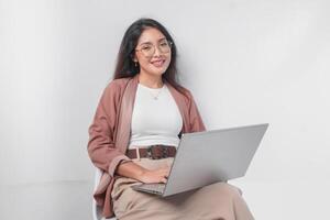 Smiling young Asian business woman sitting down and holding a laptop open over isolated white background. photo