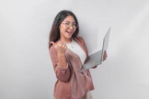 Cheerful young Asian business woman showing thumbs up and holding laptop on isolated white background. photo