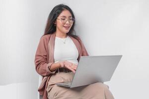 sonriente joven asiático negocio mujer sentado abajo y participación un ordenador portátil abierto terminado aislado blanco antecedentes. foto