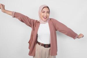 Cheerful Asian Muslim woman wearing hijab dancing with excited expression and having fun gesture over isolated white background. photo