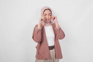 Sad beautiful Asian Muslim woman in hijab crying and wiping tears on cheek over isolated white background. photo