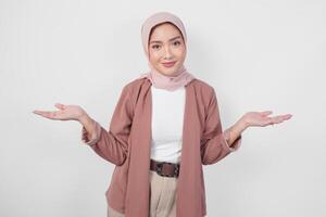 Smiling young Asian Muslim woman wearing hijab presenting copy space on her right and left side over isolated white background. photo