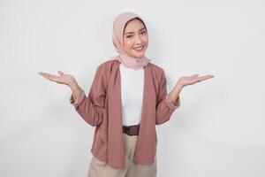 Smiling young Asian Muslim woman wearing hijab presenting copy space on her right and left side over isolated white background. photo