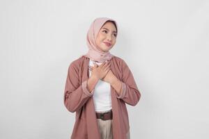 Happy mindful thankful young Asian Muslim woman wearing hijab hands on chest smiling isolated on white background. photo