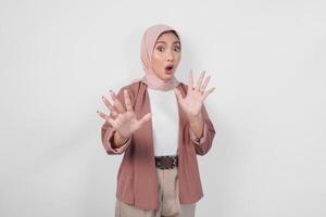 Displeased Asian woman wearing hijab gesturing a refusal or rejection sign, saying no, asking to stop using hands, standing over isolated white background. photo