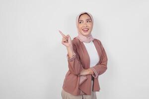 Happy young Asian Muslim woman wearing hijab pointing to the copy space on her left and right side, isolated by a white background. photo