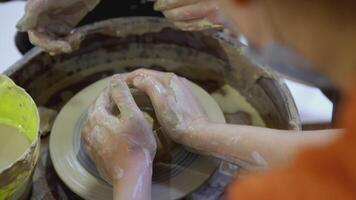 The hands of an adult and a child in close-up are engaged in pottery at the ART festival. The hands of a child on a potter's wheel sculpt a pot. The master teaches the child the skill of creating video