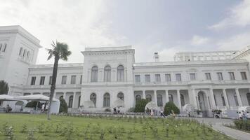 Livadia Palast. Aktion. das Festung im Jalta ist gemacht von rein Weiß Stein Nächster zu Palme Bäume und ein Straße wo Menschen gehen und hinter ein schön Blau Himmel. video