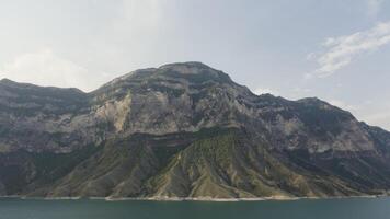 aéreo Visão enorme montanhas com crescendo árvores Ação. verão Colina e turquesa rio em nublado céu fundos. video