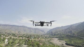 Quadcopter hängend im das Luft über Grün Senke und wachsend Bäume. Aktion. Drohne mit Spinnen Klingen über Berge auf wolkig Himmel Hintergründe. video