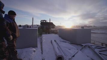 MOSCOW, RUSSIA - FEBRUARY 25, 2022 . Men watch as a bulldozer takes away a heavy thing. CLIP. In the north, heavy equipment carries weights. Blue sky and white snow behind large machinery video
