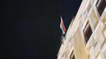 bas vue de bâtiment avec drapeau à nuit. action. bâtiment avec drapeau sur Contexte de nuit ciel. magnifique neige chutes à illuminé bâtiment à nuit video