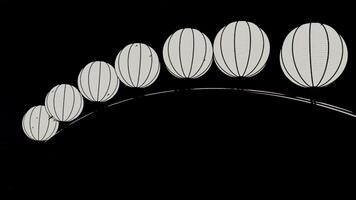 kinesisk papper svartvit lyktor hängande i en rad på en svart bakgrund. design. 3d sfärisk form lyktor svängande i de vind under regn droppar. video