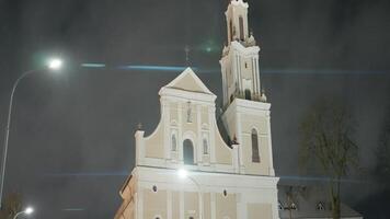 oud Katholiek kerk in nacht stad. actie. mooi licht tempel verlichte Bij nacht. Katholiek kerk met toren in modern stad video