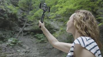 Frau nimmt schön Berg Ansichten auf Telefon mit Stabilisator. Aktion. Fachmann Schießen auf Telefon mit stabilisierend Handheld Stativ. Handbuch Stabilisator zum Fachmann draussen Schießen video