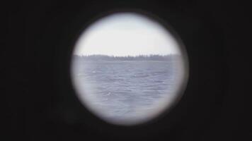 View from the round porthole of the ship on the landscape. CLIP. The coast covered with trees by which a ship sails on a calm sea video