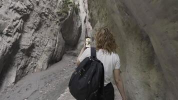 achterzijde visie van een jong vrouw wandelen in kloof tussen rotsen met een telefoon in haar handen. actie. vrouw reiziger het schieten mooi natuurlijk steen vorming. video