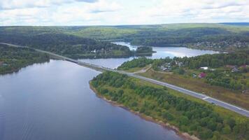 From a bird 's - eye view . Clip. A long bridge over a calm river with cars and green vegetation in the background and blue clouds . video