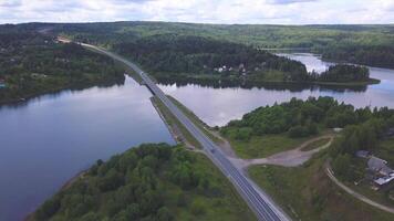 From a bird 's - eye view . Clip. A large green forest with a bridge on which cars drive passing through the river with a cloudless sky in the background. video