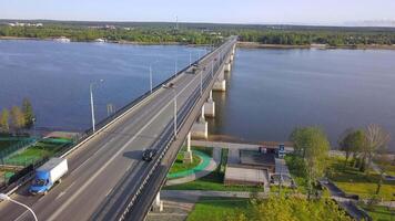 View from the height . Clip. A large long bridge over the river on which cars drive and there are lights behind the bridge you can see a green city with small residential buildings and a large forest video