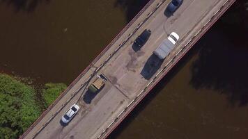 A small bridge over the river. Clip. The view from the drone. A narrow river through which there is a high bridge on which cars drive next to green grass and trees . video