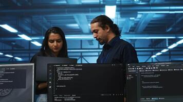 Developer in server hub using laptop to present manager plan of repairing equipment storing datasets. Specialist uses notebook to explain team leader ways of fixing rigs doing computational operations video
