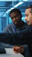 Vertical Multiracial engineers programming in high tech facility with server rows providing computing resources for different workloads. Diverse coworkers supervising data center supercomputers video