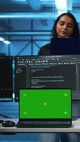 verticaal groen scherm laptop in gegevens centrum in voorkant van manager en het ondersteuning specialisten werken samen, toezien op server rijen. team leider en medewerkers toezicht houden op supercomputers gebruik makend van mockup notitieboekje video