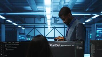 Manager uses tablet, supervising team programming servers providing computing resources for different workloads. Inspector using device to oversee engineers in data center mending supercomputers video