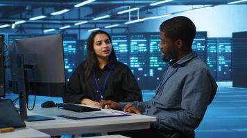 Multiracial team of IT engineers in server room brainstorming ways to fix equipment storing datasets. Indian and african american coworkers discussing how to mend racks doing computational operations video
