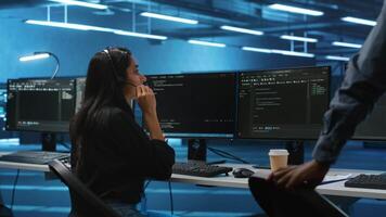 Team of IT support experts working together, supervising server rows in computer network security data center. Woman next to colleagues talking in headphones mic while overseeing supercomputers video