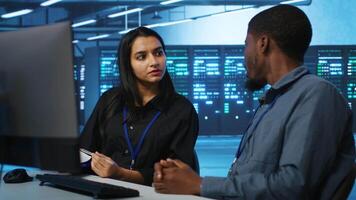 Coworkers in data center looking over annual systems review documents, discussing about parameters. Colleagues doing brainstorming in high tech workspace, talking about server clusters specs video