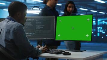 IT technician looking at green screen PC, working in data center, ensuring optimal performance. Man monitoring energy consumption across operational server rigs components using chroma key monitor video