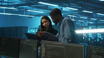 Coworking technicians looking at laptop screen, working in data center, ensuring optimal performance. Colleagues monitoring energy consumption across server rigs components, doing brainstorming video