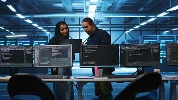 Multiracial colleagues in server hub workspace collaborating to fix servers providing computing resources for workloads. Engineers doing brainstorming while supervising data center supercomputers video