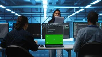 Multiethnic engineers working in high tech server hub, using green screen laptop and PCs to analyze data. Diverse employees examining infrastructure in data center, using chroma key notebook video