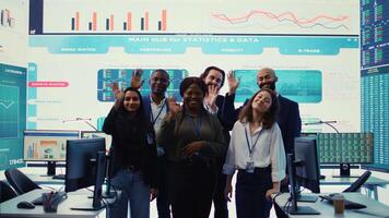 Confident smiling enterprise team uniting their forces to improve workflow and efficiency, achieve organizational goals. Diverse group of analysts work in telecommunications control room. Camera B. video